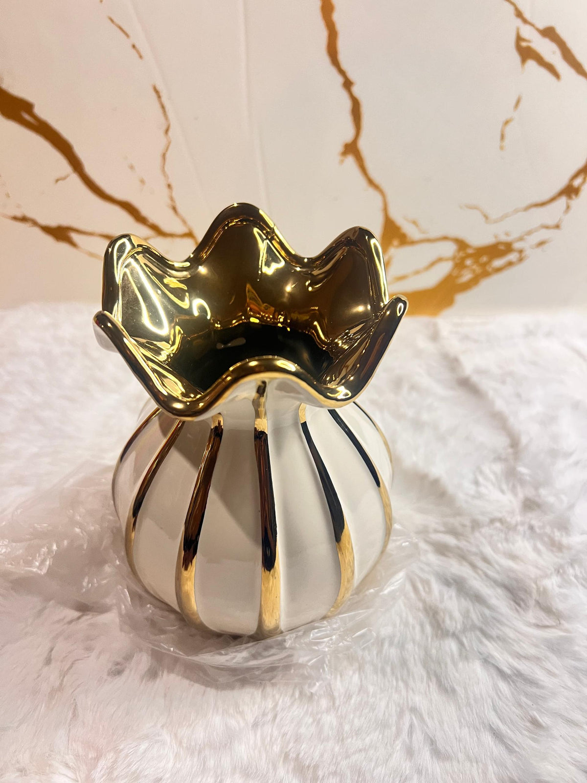A decorative ceramic vase with a glossy white body, vertical gold and black stripes,