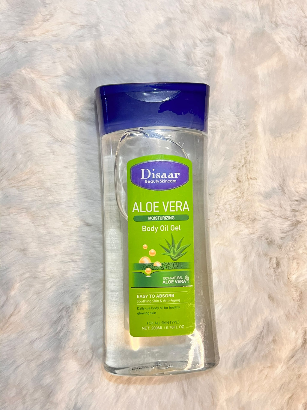 A bottle of Disaar Aloe Vera Body Oil Gel with a blue cap and green label, placed on a white faux fur surface.