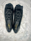 A pair of black patent leather ballet flats with quilted insoles and a bow on the toe, displayed on a white textured faux fur surface. The insole features a gold 'Fashion' logo.