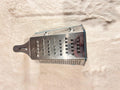 A stainless steel box grater with a dark gray handle