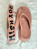 A pair of chunky platform flip-flop sandals in a dusty pink color, featuring a thick sole and a strap with the text 'JWKHSIH' in black, displayed on a white faux fur background.