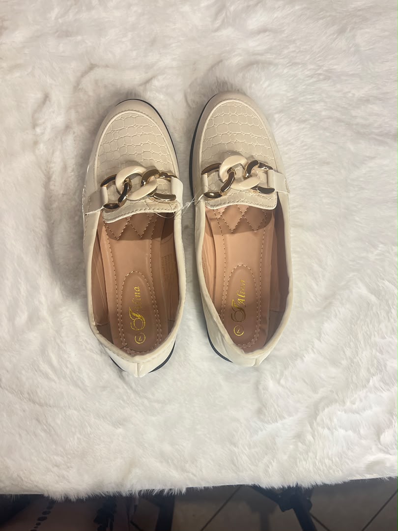 cream-colored loafers with a textured toe cap and a chunky gold-tone chain