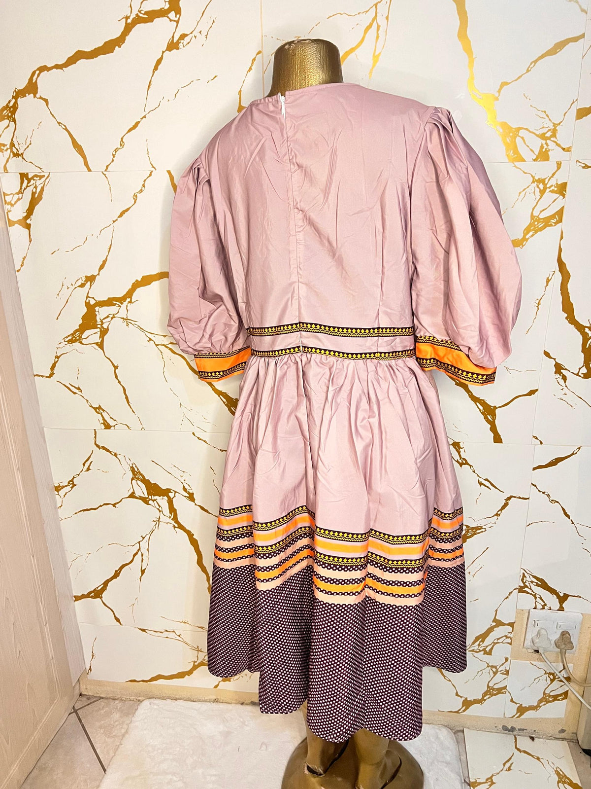Pink dress has puff sleeves, a split neckline with decorative trim, a patterned waistband