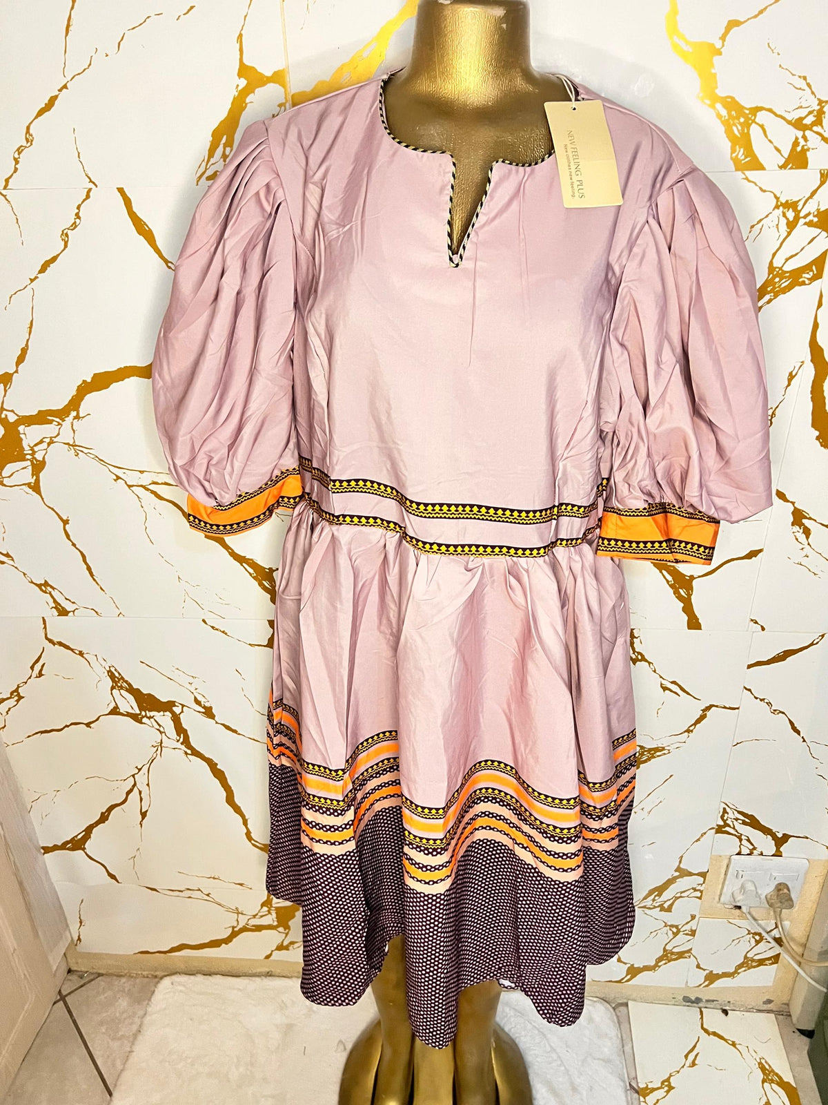 Pink dress has puff sleeves, a split neckline with decorative trim, a patterned waistband