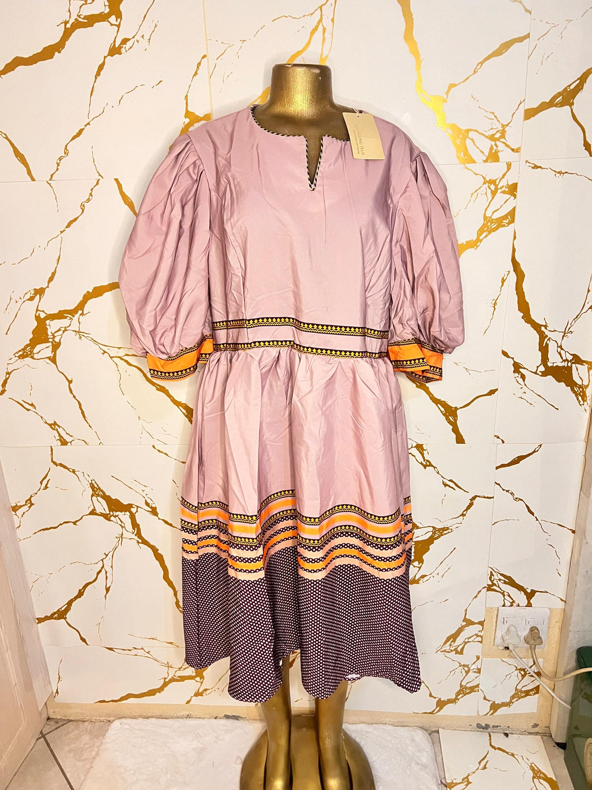 A pink dress has puff sleeves, a split neckline with decorative trim, a patterned waistband