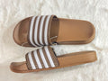 A pair of Adidas slide sandals with brown and white stripes, shown from a top-down view on a white faux fur background.