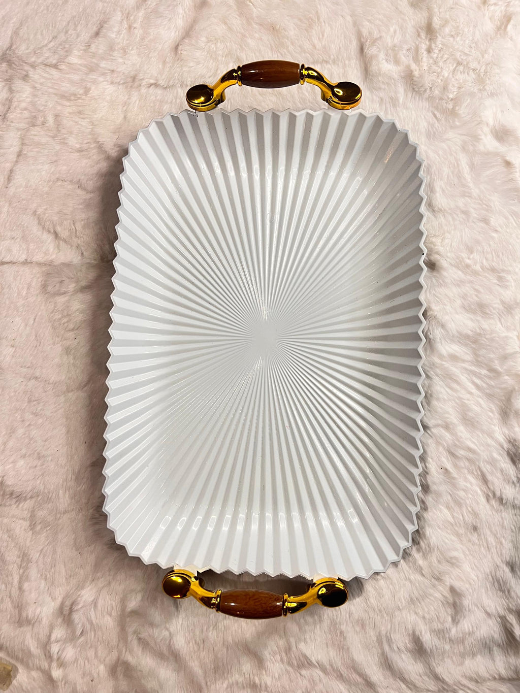 A white rectangular serving tray with a fluted, sunburst pattern and ornate gold handles with brown accents