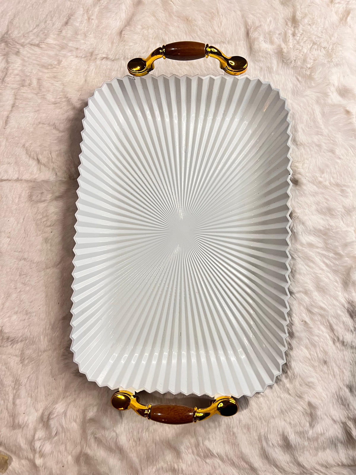 A white rectangular serving tray with a fluted, sunburst pattern and ornate gold handles with brown accents
