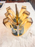 A gold-toned glass wine decanter set arranged in a circular cluster on a white faux fur surface, with a vertical gold metal rod standing in the center.