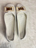 A pair of white leather ballet flats with a prominent gold-tone rectangular buckle detail on the toe, displayed on a white faux fur surface.