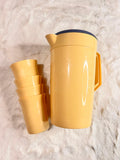 A yellow plastic thermal water bottle with a dark blue lid, shown next to a stack of four matching yellow cups on a white faux fur surface.
