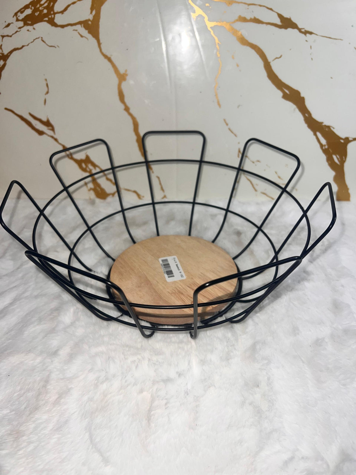A black metal wire fruit basket with a round light wood base