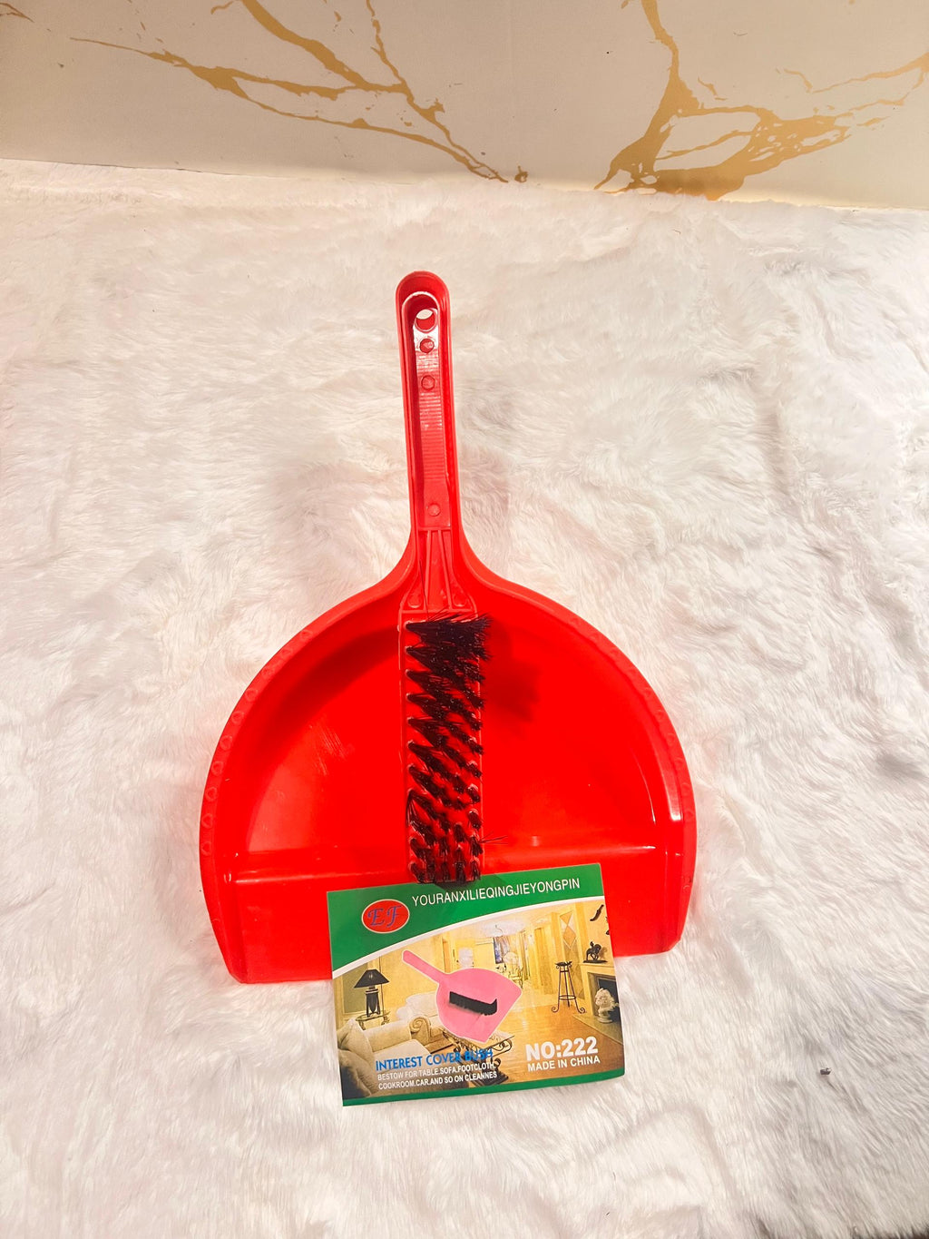A red plastic dustpan with an integrated black wire brush on the front