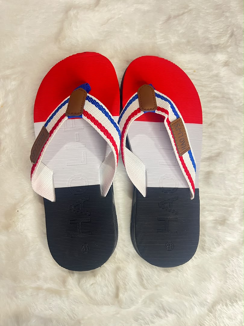 A pair of red, white, and navy blue flip-flop sandals with brown straps, laid flat on a white faux fur surface.
