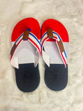 A pair of red, white, and navy blue flip-flop sandals with brown straps, laid flat on a white faux fur surface.