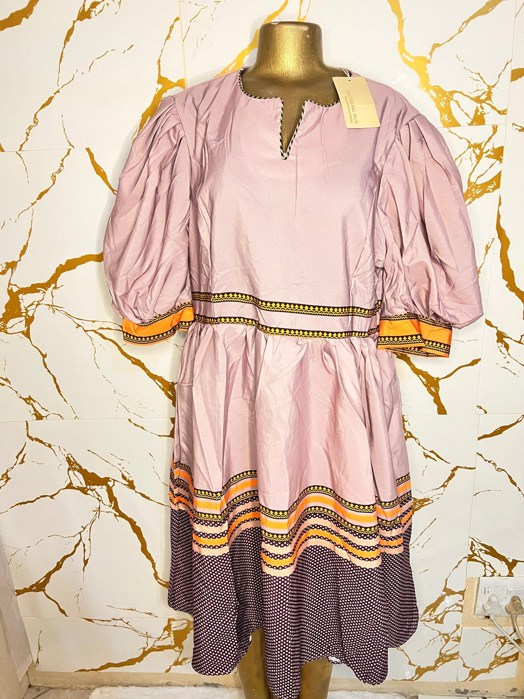 Pink dress has puff sleeves, a split neckline with decorative trim, a patterned waistband