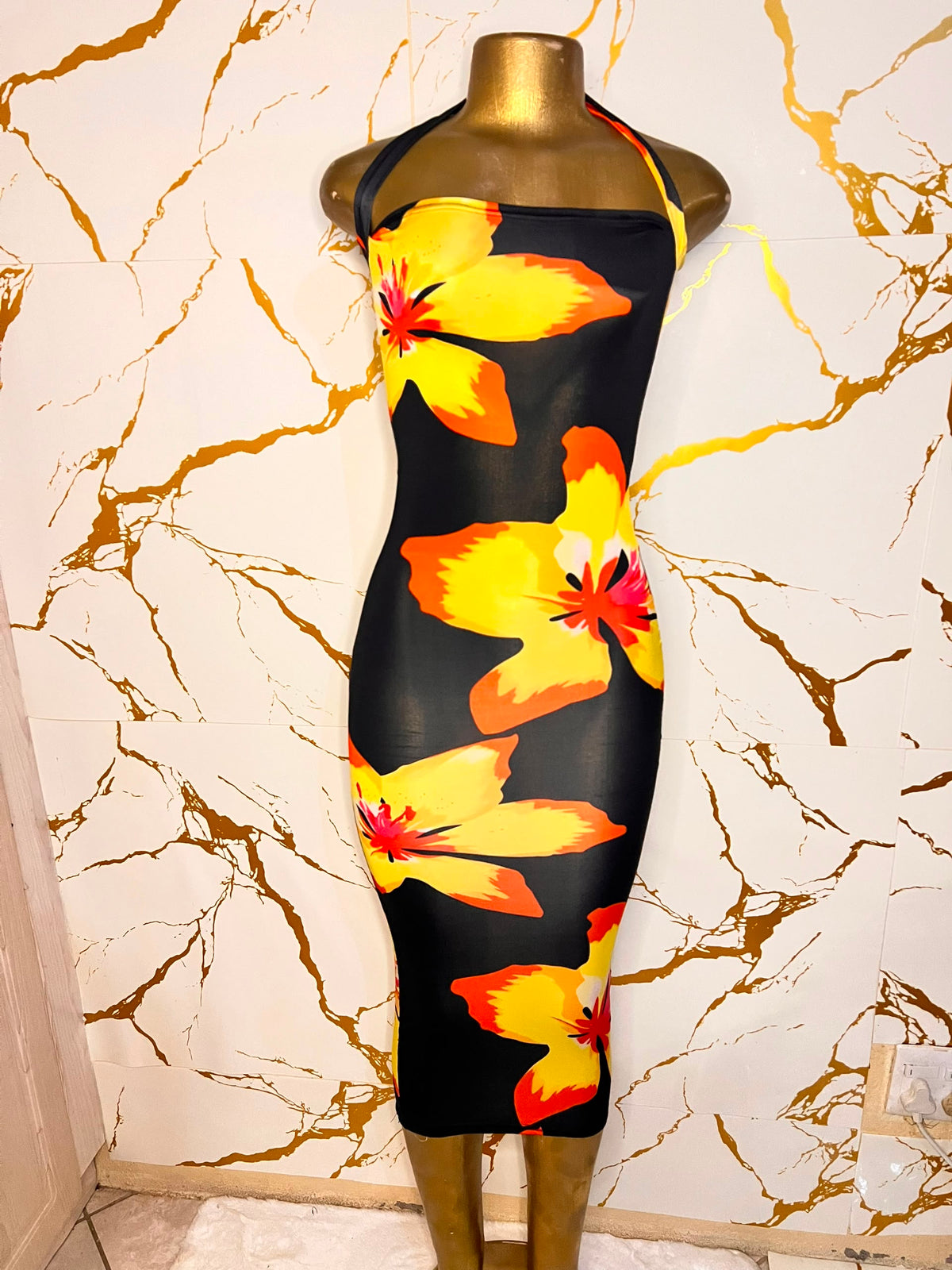 A black halter-neck bodycon dress with a vibrant yellow, orange, and red hibiscus floral print