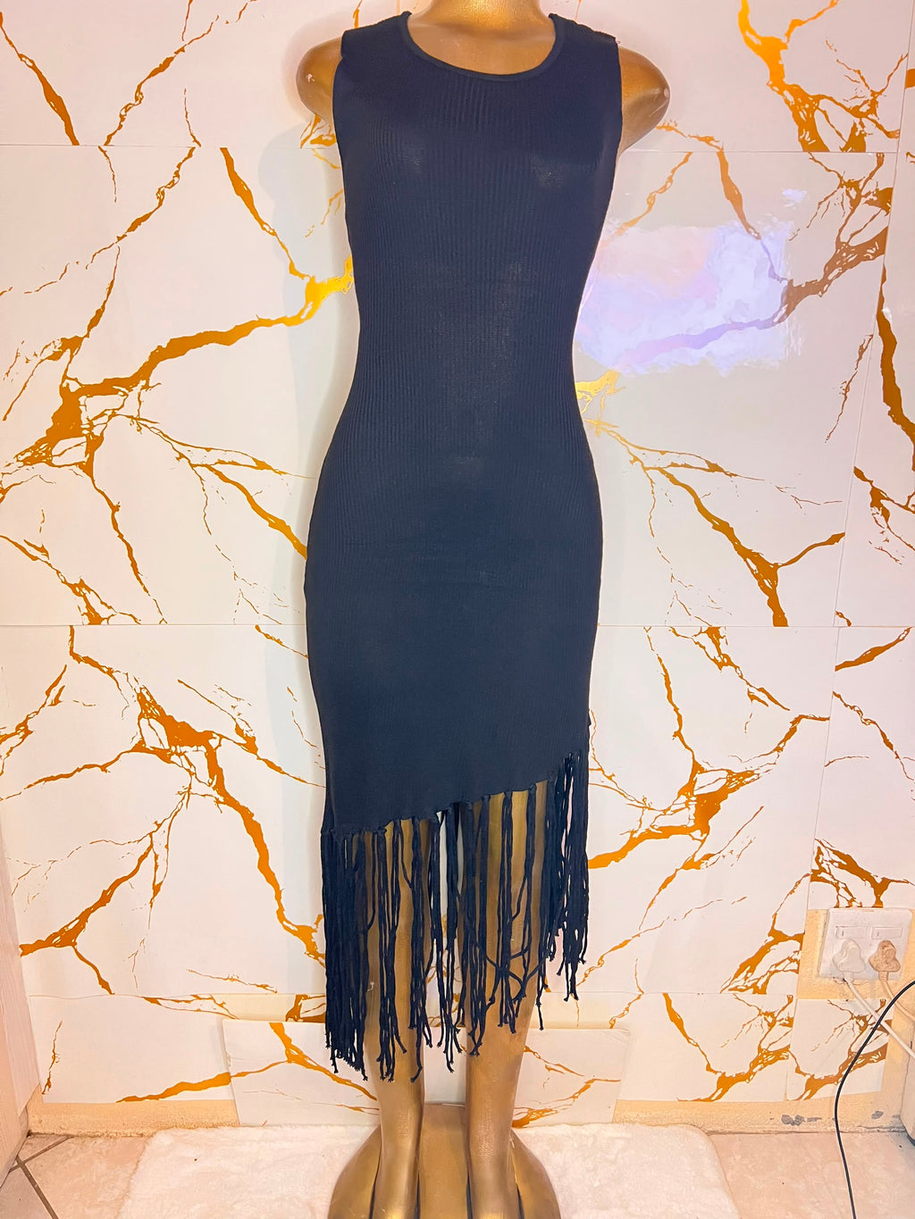 A sleeveless ribbed knit bodycon dress in black with a fringe hem,