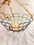 A black metal wire fruit basket with a round light wood base