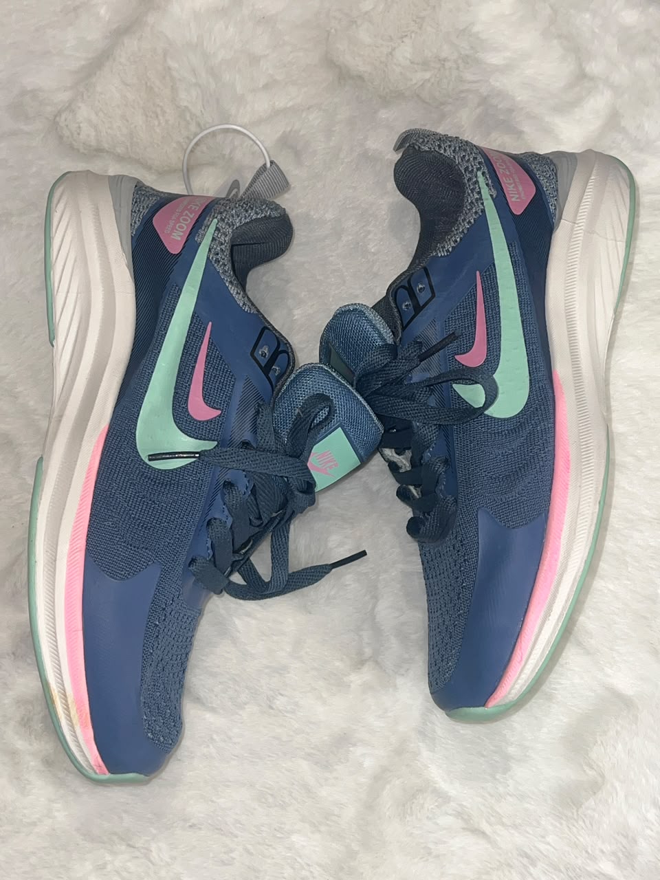 A pair of Nike running shoes in navy blue with mint green and pink accents, displayed on a white faux fur surface.