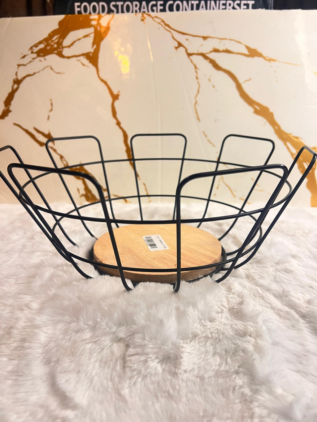 A black metal wire fruit basket with a round light wood base