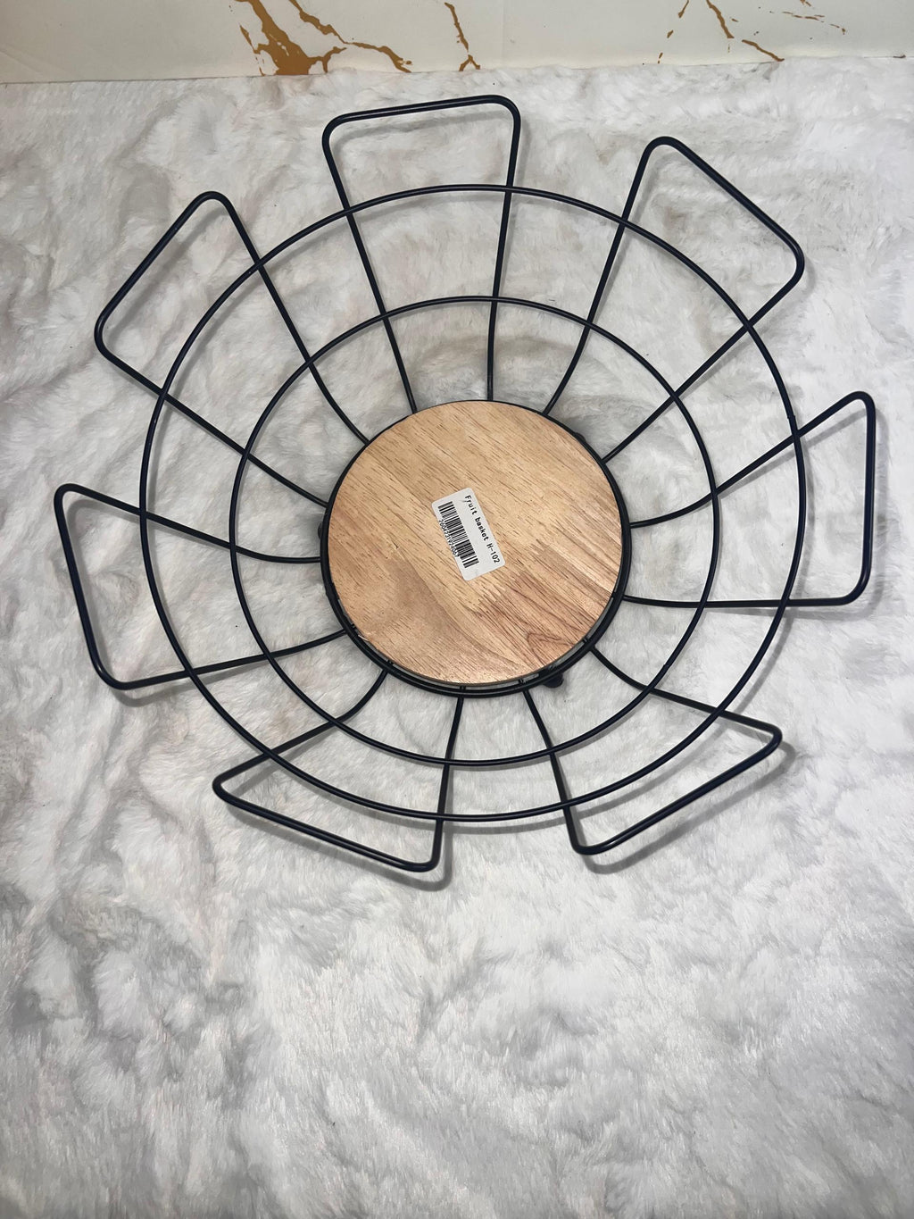 A black metal wire fruit basket with a round light wood base