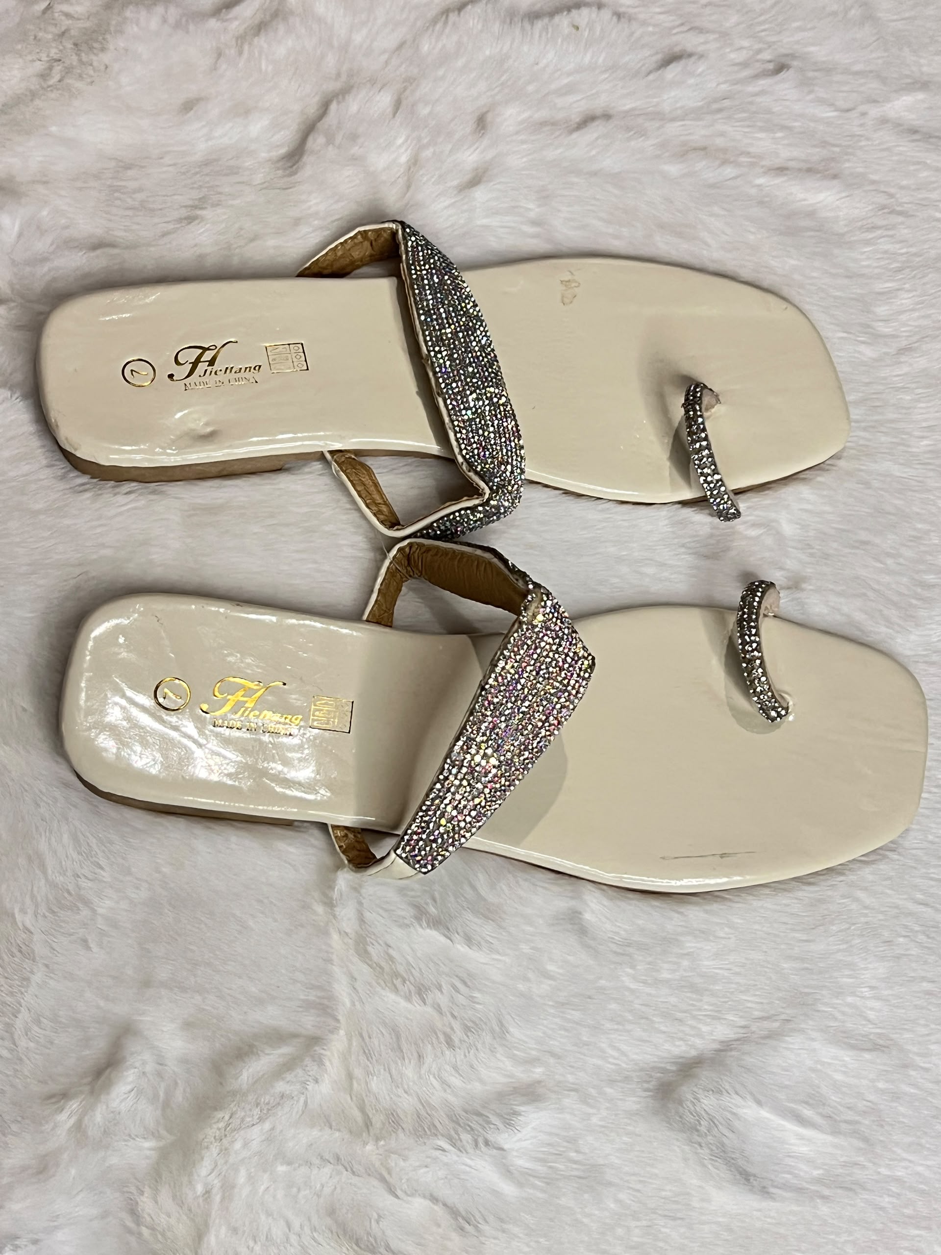 A pair of women's slide sandals with cream-colored feetbeds and sparkling silver rhinestone straps, displayed on a white faux fur background. The brand name 'Havanna' is visible on the insole.