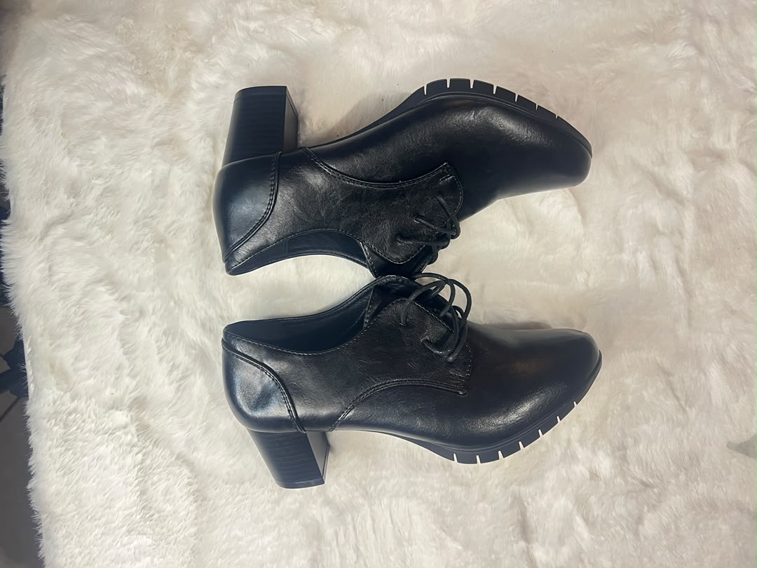 A pair of black leather lace-up ankle boots with block heels, displayed on a white faux fur surface.