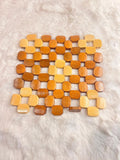 A square wooden bead mat made of small octagonal wooden beads in various natural wood tones, laid flat on a white faux fur surface.