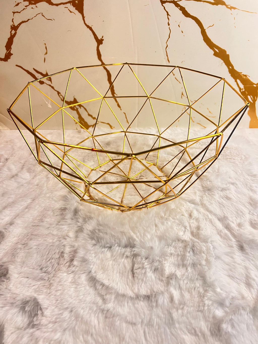 A gold geometric wire bowl with a faceted triangular pattern.