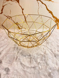 A gold geometric wire bowl with a faceted triangular pattern.