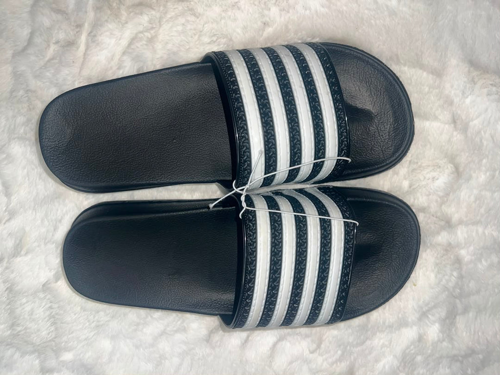 A pair of Adidas slide sandals with black footbeds and white stripes on the straps, laid flat on a white textured rug.