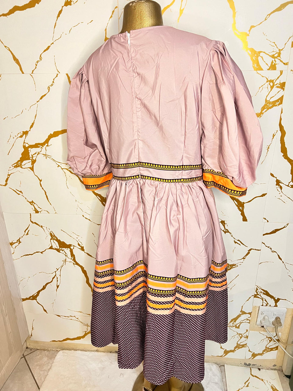 Pink dress has puff sleeves, a split neckline with decorative trim, a patterned waistband