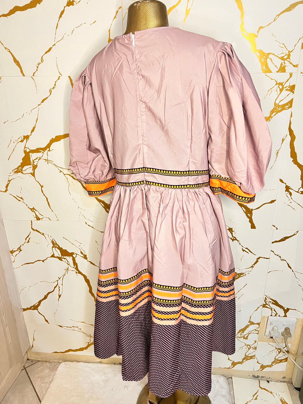 Pink dress has puff sleeves, a split neckline with decorative trim, a patterned waistband