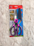 A pair of kitchen shears and a knife blade set in retail packaging, featuring metallic silver blades and handles with pink and purple accents, displayed on a white faux fur surface.
