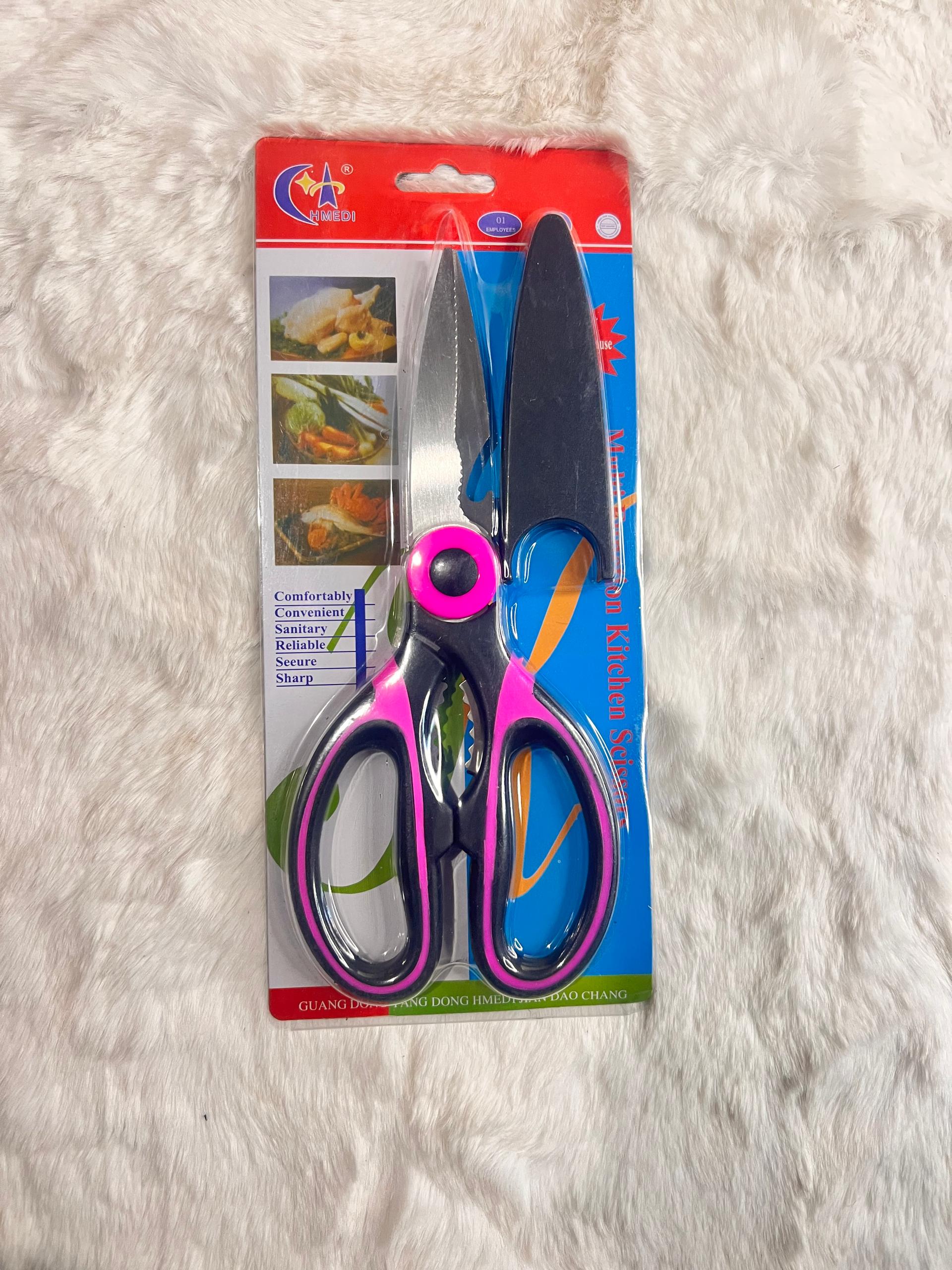 A pair of kitchen shears and a knife blade set in retail packaging, featuring metallic silver blades and handles with pink and purple accents, displayed on a white faux fur surface.