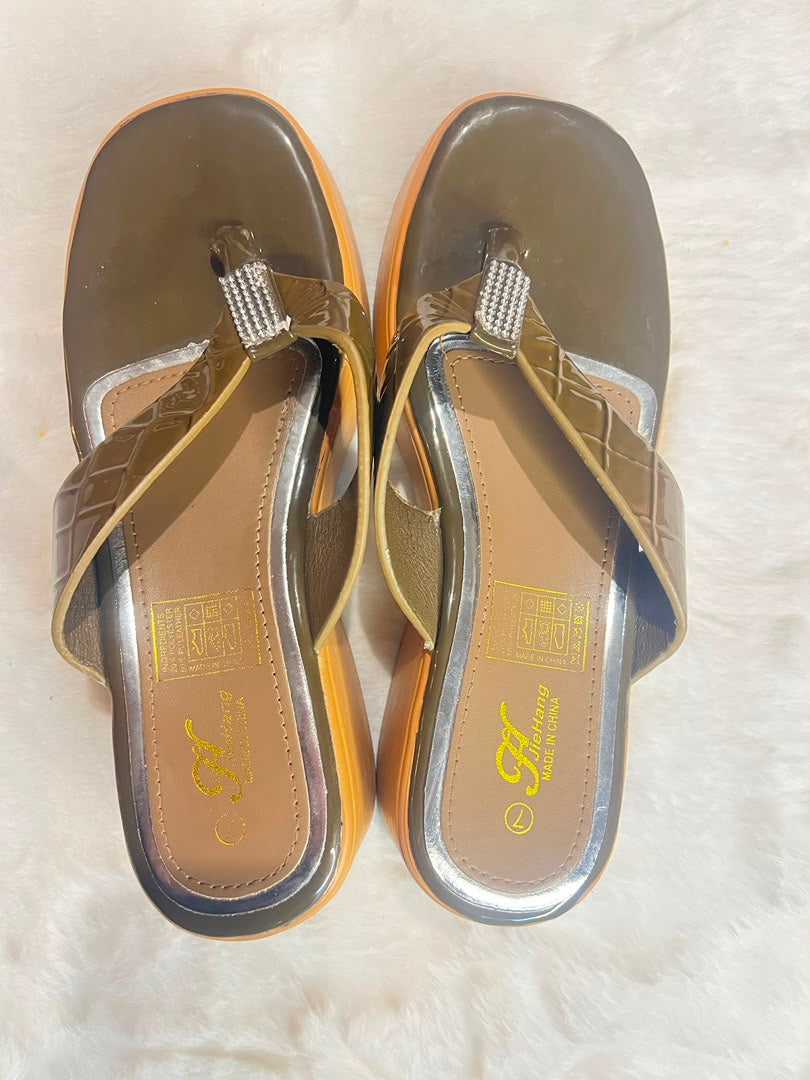 A pair of women's thong sandals with metallic bronze and gold straps, featuring a rhinestone-embellished toe post and a textured sole, displayed on a white faux fur surface.